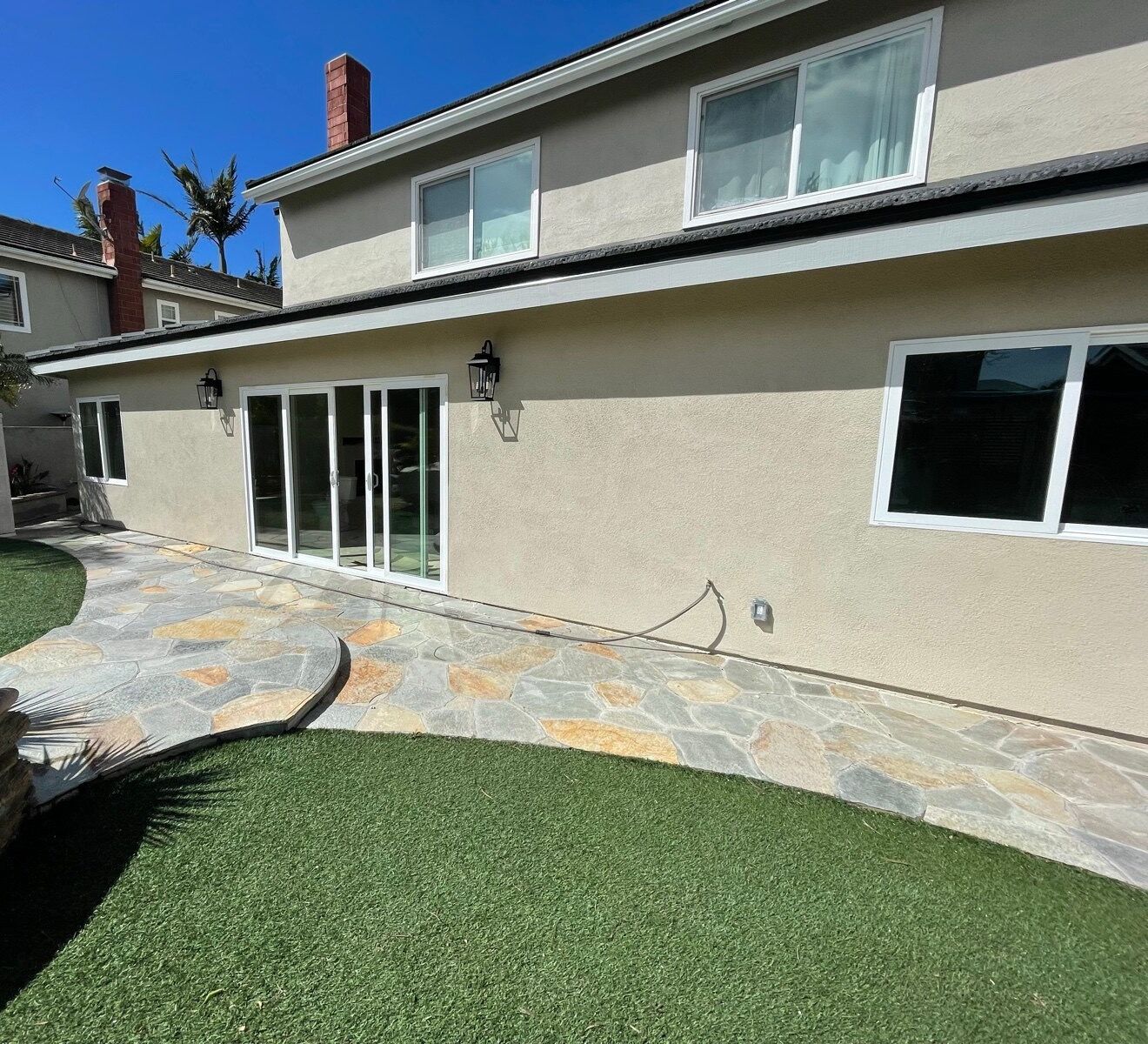 Finished rear of the Huntington Beach addition: sliding doors, stucco and a flagstone patio under a blue sky