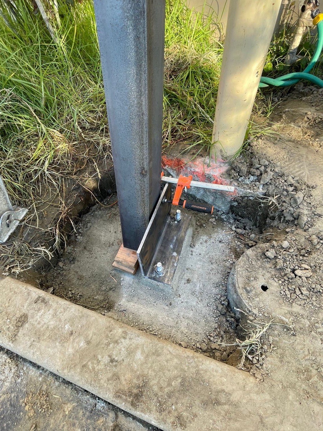 A steel column welded to its base plate at grade, beside an existing post